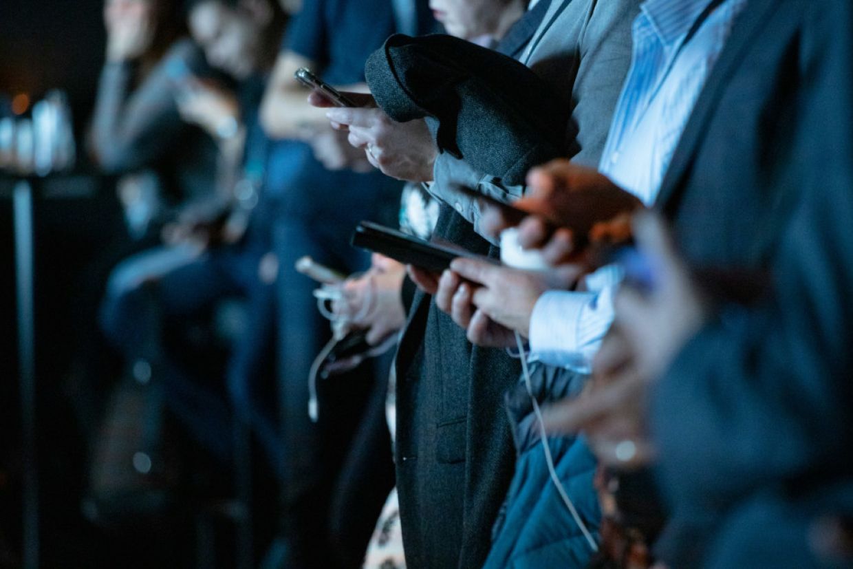 A row of people are occupied by their smartphones.