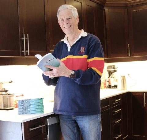 Man standing in a kitchen wearing a Queen's rugby shirt.