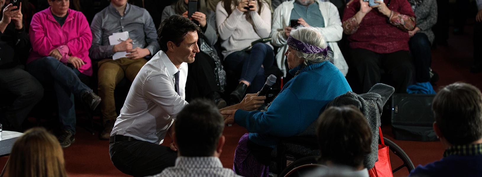 Prime Minister Justin Trudeau kneels on the floor to take a question from Laurel Claus-Johnson, who sits in a wheelchair, during a town hall in Kingston in January 2017.