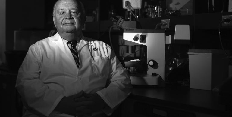 A man wearing a lab coat sits in front of a microscope.