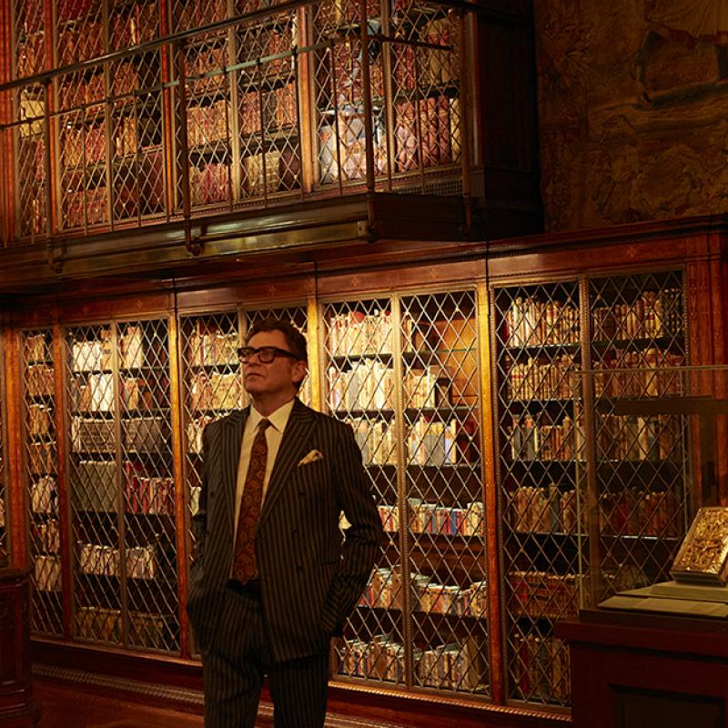 Man standing in a library wearing a suit and glasses.