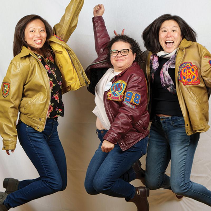 Three alumni jump in the air wearing their Queen's jackets
