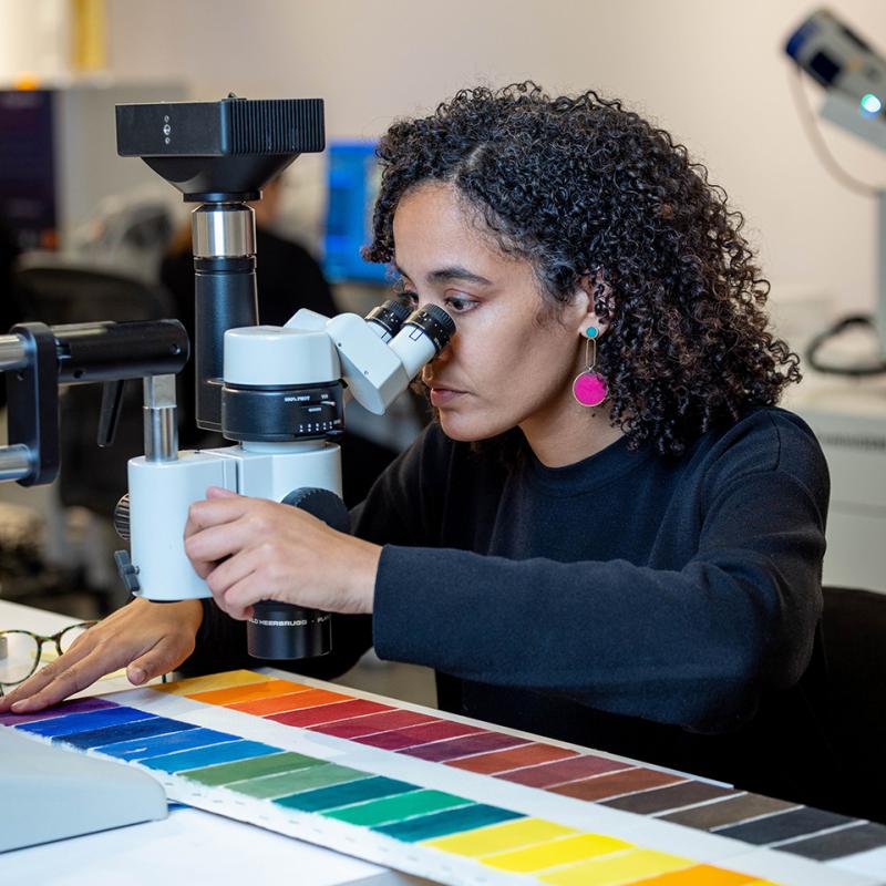 Woman looking through a microscope at a series of painted colour blocks