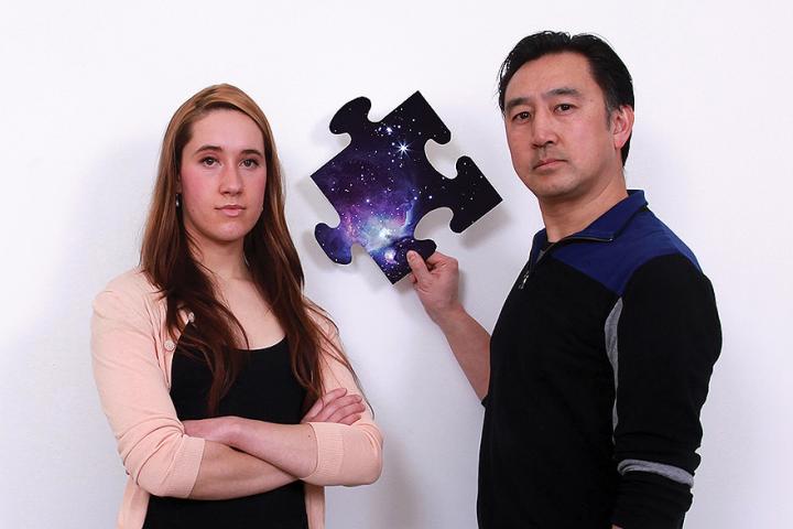 Jennifer Mauel and Mark Chen, holding a puzzle piece with a solar system image on it, posing for the camera.