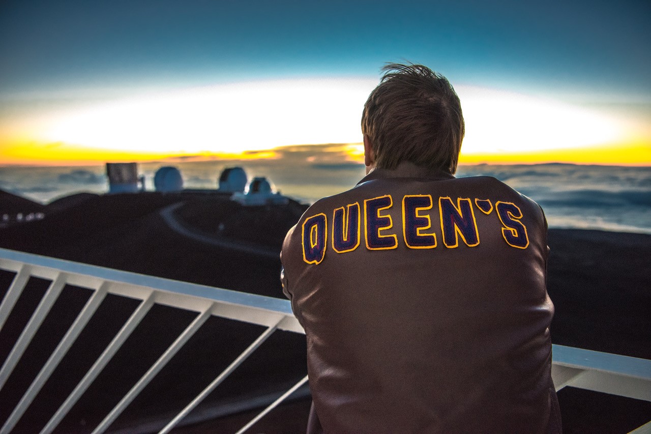 Student wearing a Queen's jacket looking out at the sunrise.