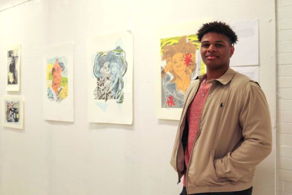 Student standing in front of visual art portraits hung on a wall.