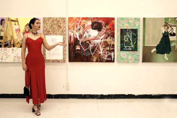 visual arts student in red dress standing in front of portraits and pictures