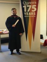 A graduate next to a 175th anniversary of Queen's University banner