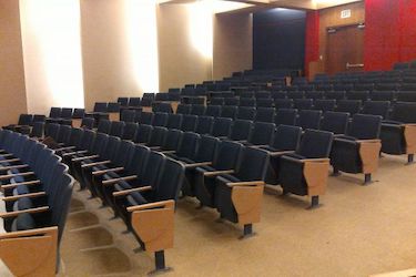 rows of fixed blue chairs in an auditorium with a red wall at the back
