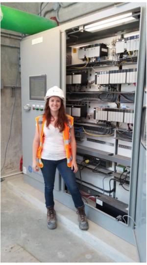 Jenn Clarke, wearing a hard hat and standing in front of a machine