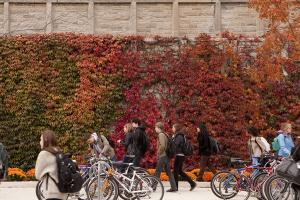Students walking past bikes parked in front of an ivy-covered Queen's building.
