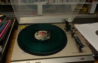 A record player holds the record, Angel Olson Big Time, a dark green transparent record with a vintage looking pink rose in the centre