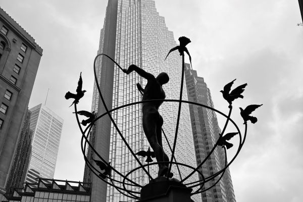 A black and white photograph of a statue in downtown Toronto featuring a man standing in the centre and doves flying around him