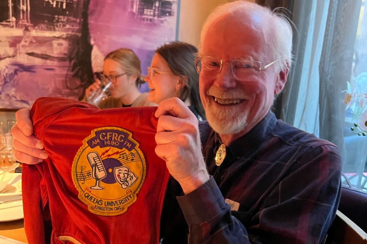 Alum smiling and holding a Queen's CFRC Radio jacket.