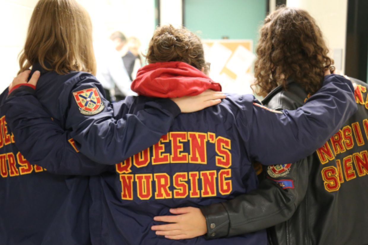 Three nursing alumni with their backs to the camera showing their jackets that read "Queen's Nursing"