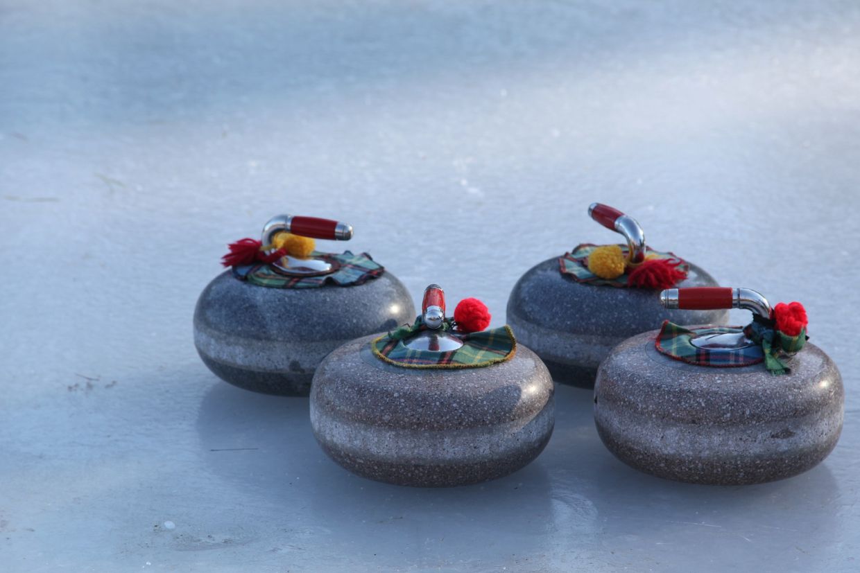 Curling rocks with tartan and pompoms on ice