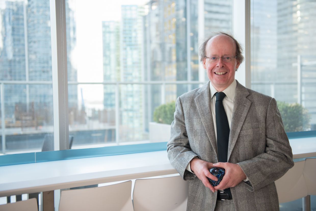 Rob Frater smiles while wearing a gray suit and holding an award in front of a cityscape. Link to event page.