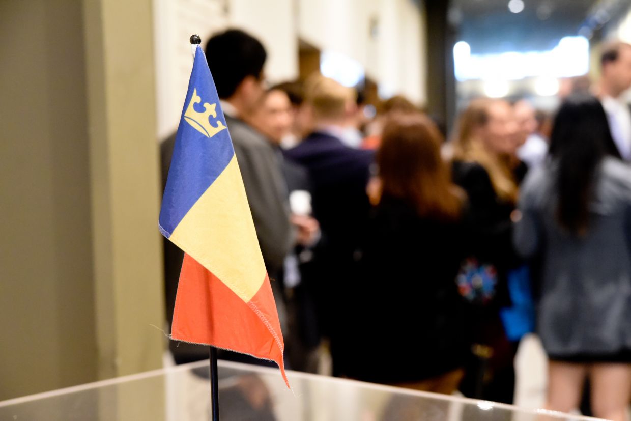 A Queen's alumni flag in the foreground with a small crowd of individuals in the background, socializing.