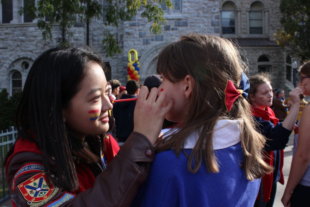 An alumnae in a Queen's jacket paints a tricolour flag on a child.