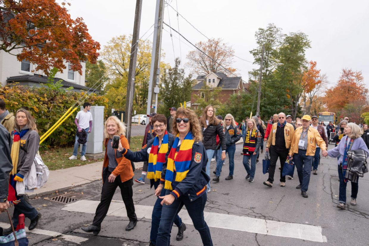Alumni walking in a parade along a street waving to the camera 