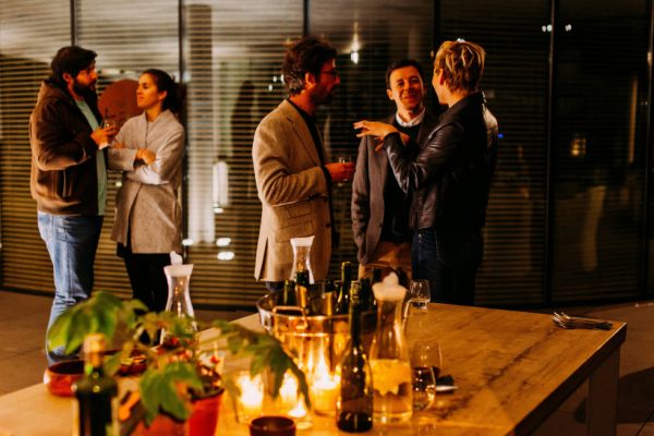 People stand in groups behind a candle lit table in conversation.