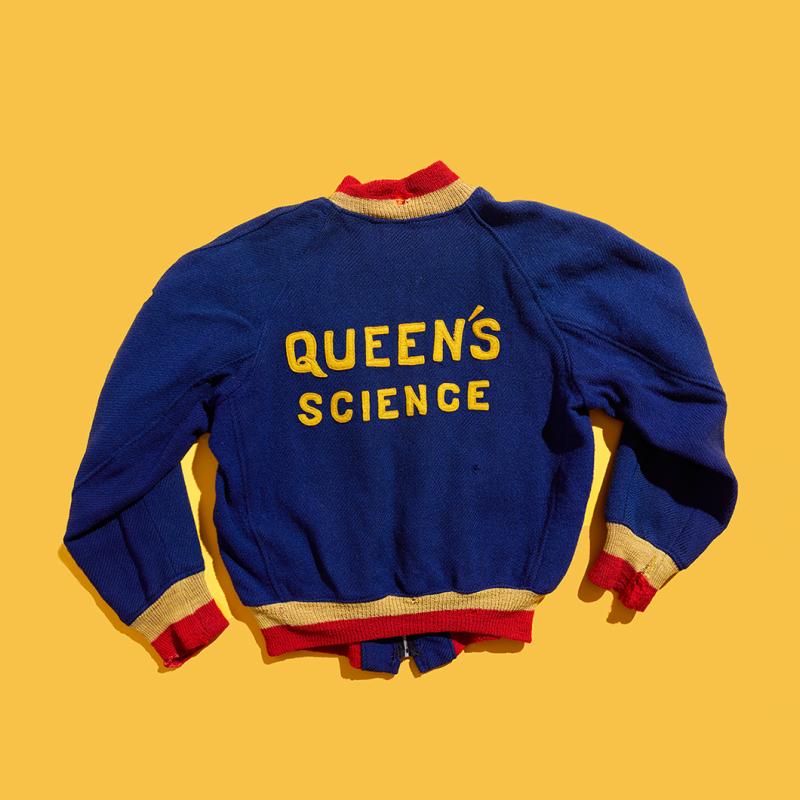 The back of wool-and-knit Queen's jacket, with Queen's science emobroidery, lies flat on a yellow background.