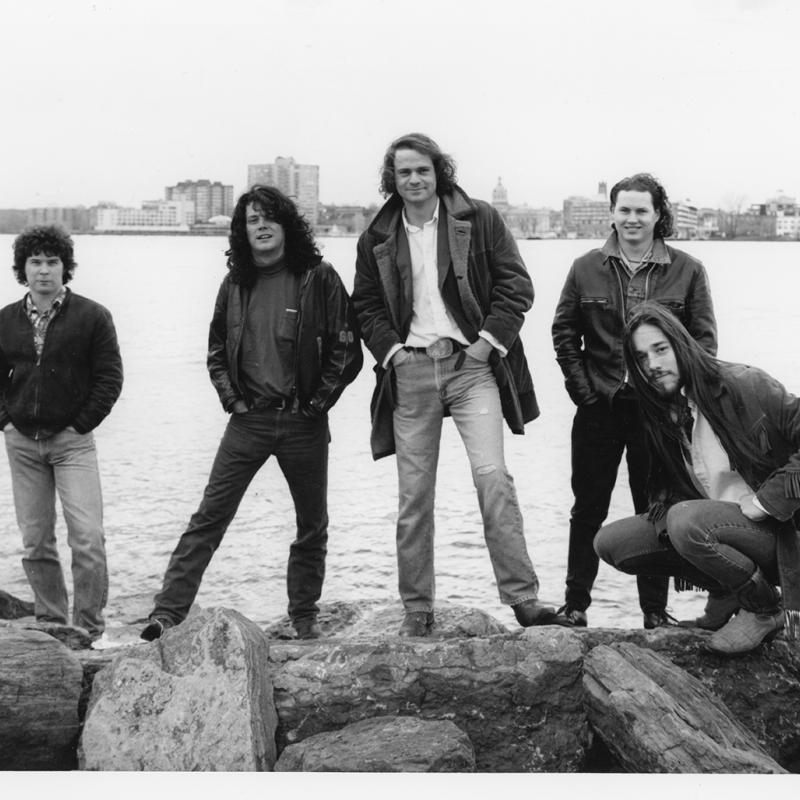 Gord Sinclair, Paul Langlois, Gord Downie, Johnny Fay, and Rob Baker pose against the Kingston skyline in the early 1990s.