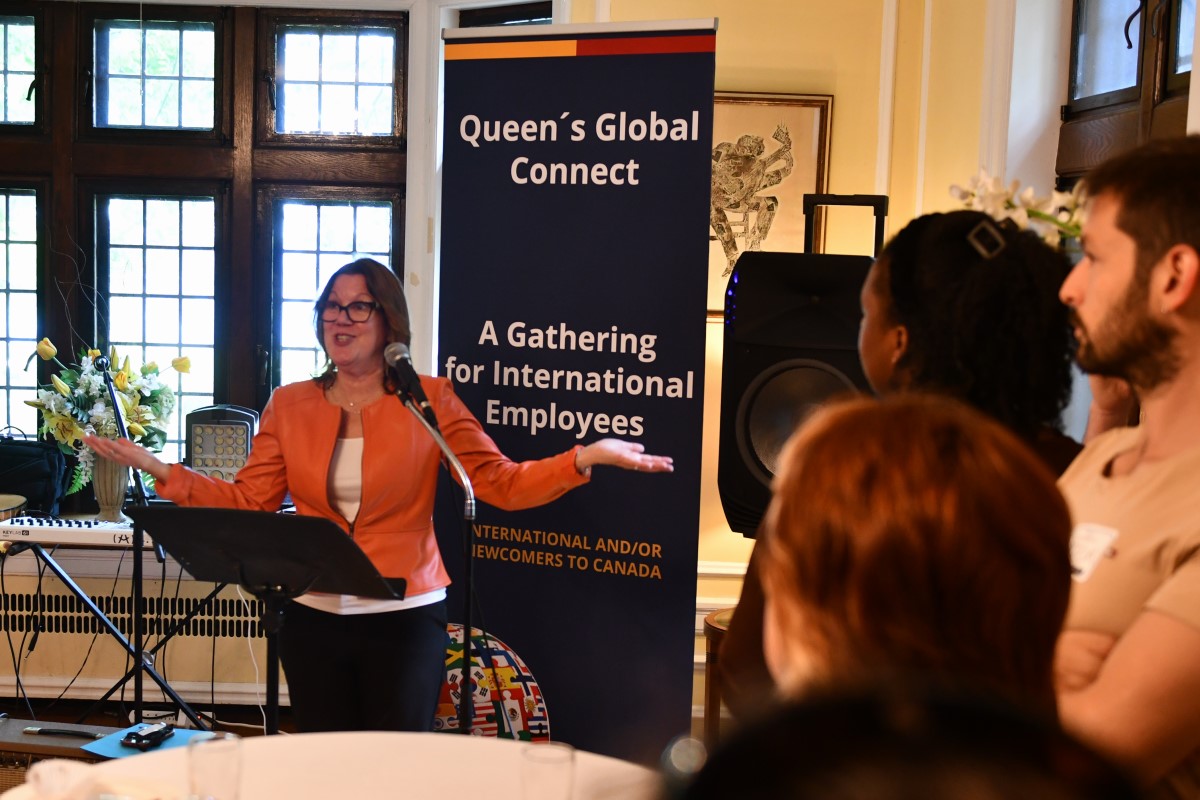 Donna Janiec, Vice-Principal (Finance and Administration), stands in front of a Queen's University banner addressing a crowd.