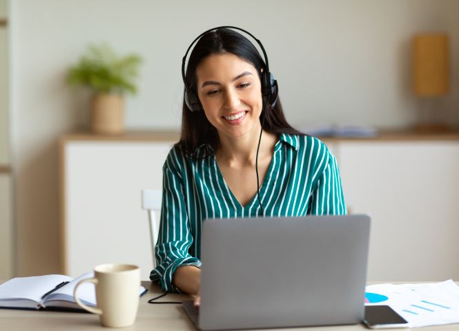 Woman sitting at a laptop with a headset on and a cup of coffee.