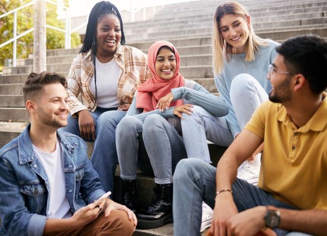 A group of people sitting on concrete stairs conversing with each other.