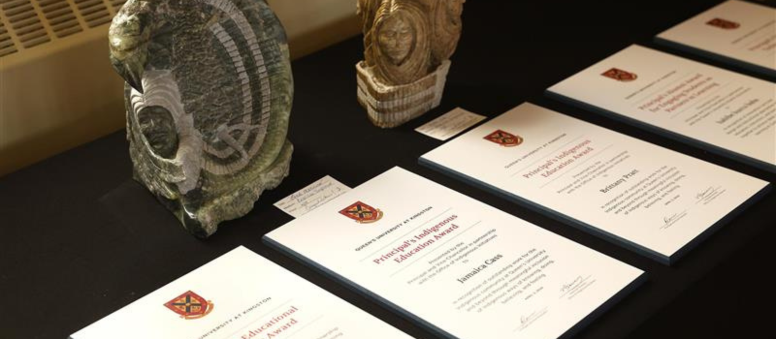 Certificates for the Principal's teaching and learning awards lined up on a table with a. black tablecloth.