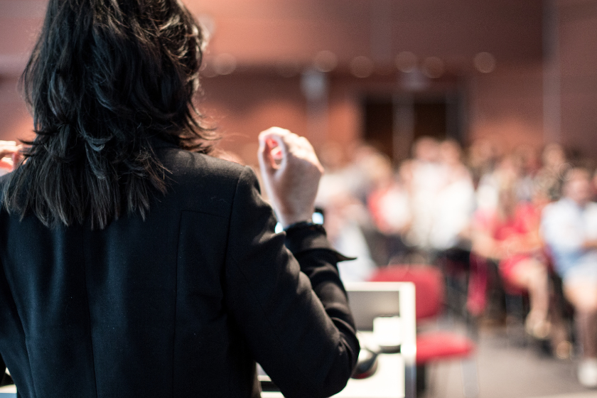 A woman speaking to a crowd from a podium.