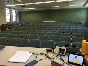 View from the front of the room: Rows of fixed chairs with tablet tables attached. The wall at the back is green and the side walls are off white.