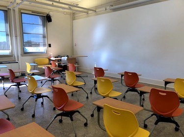 Classroom with orange and yellow movable chairs with tablet arms and whiteboard surface on the wall.