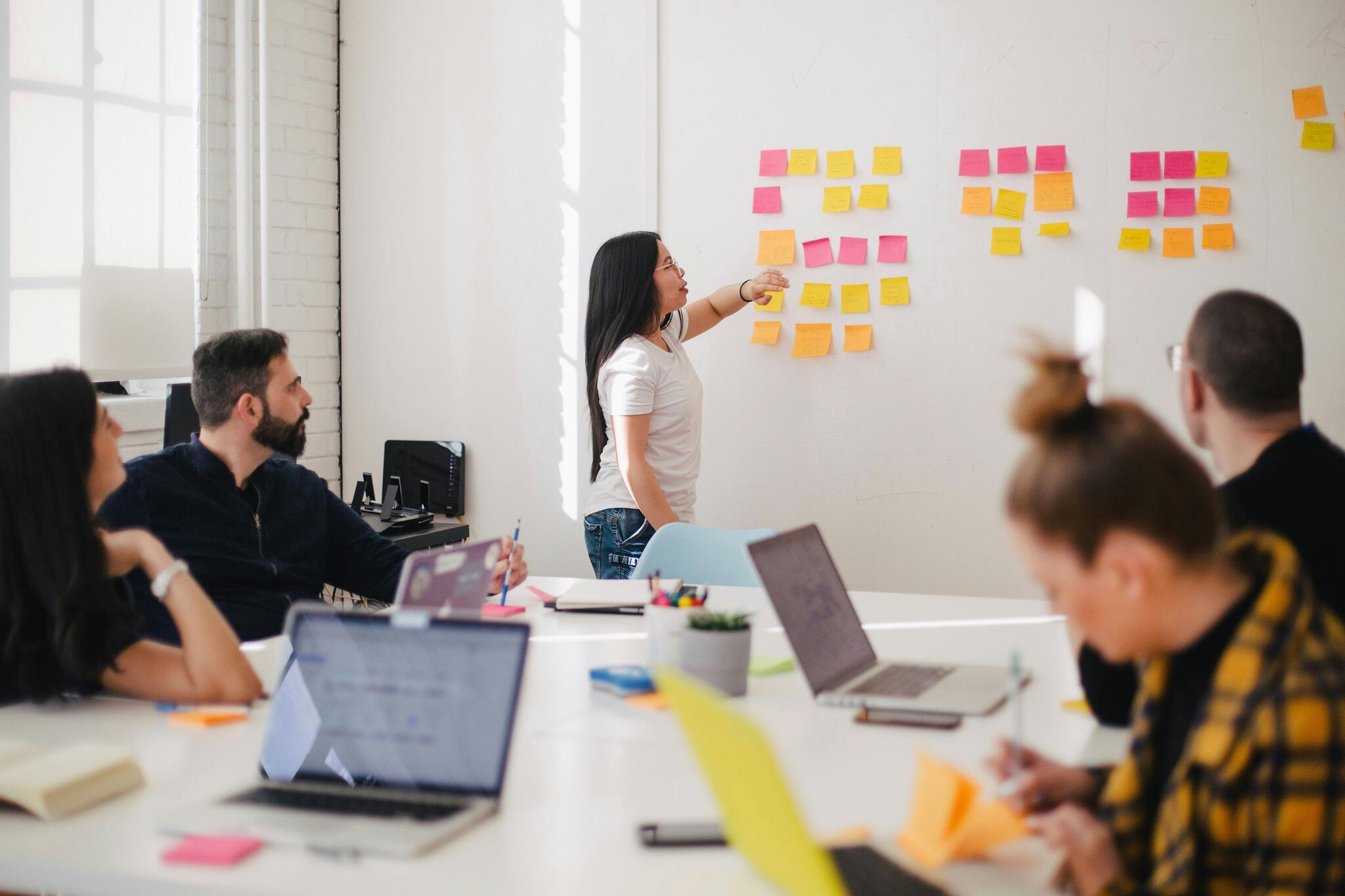 students working at a table with one standing at a wall covered in post its