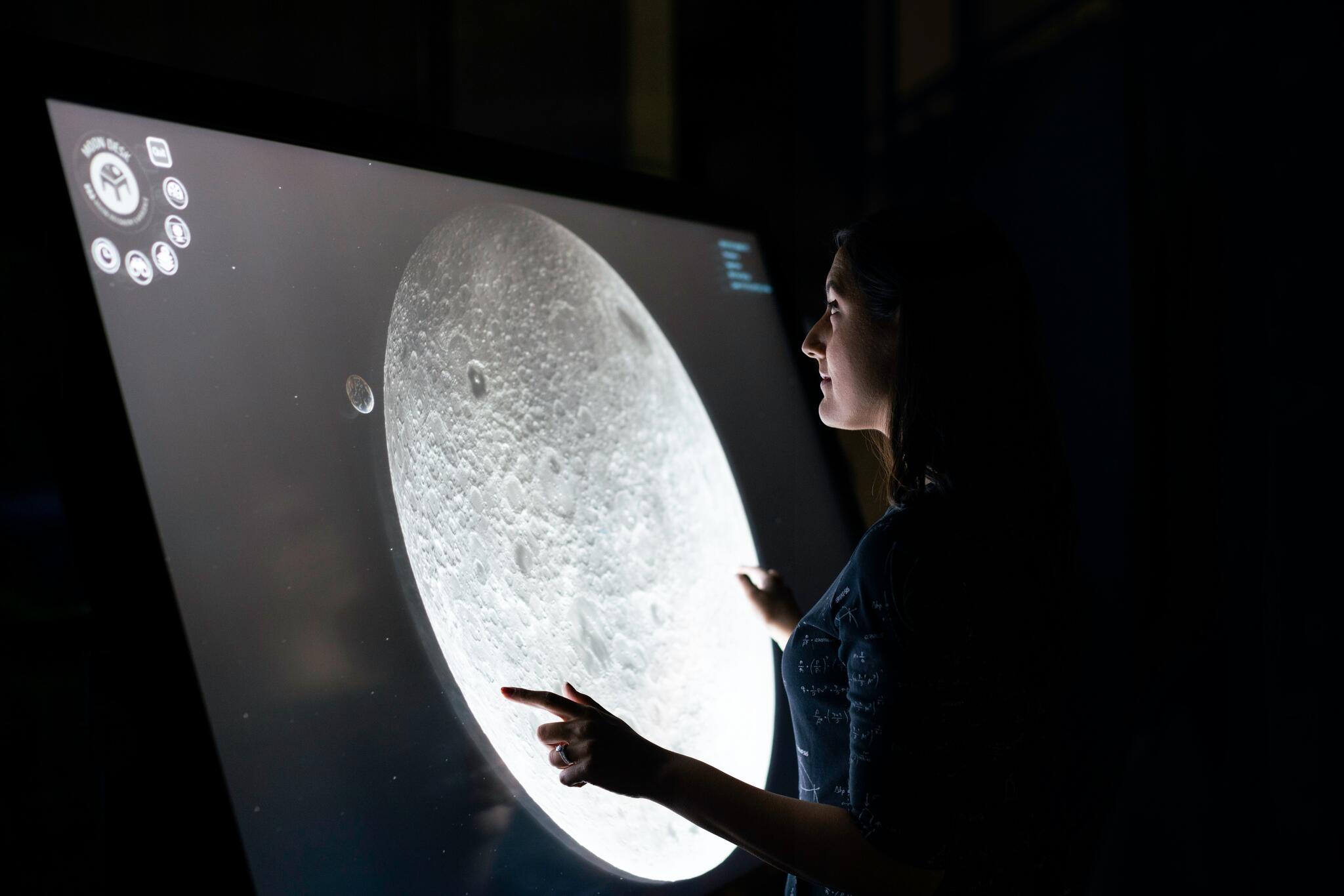 person interacting with a large screen that has an image the moon on it.