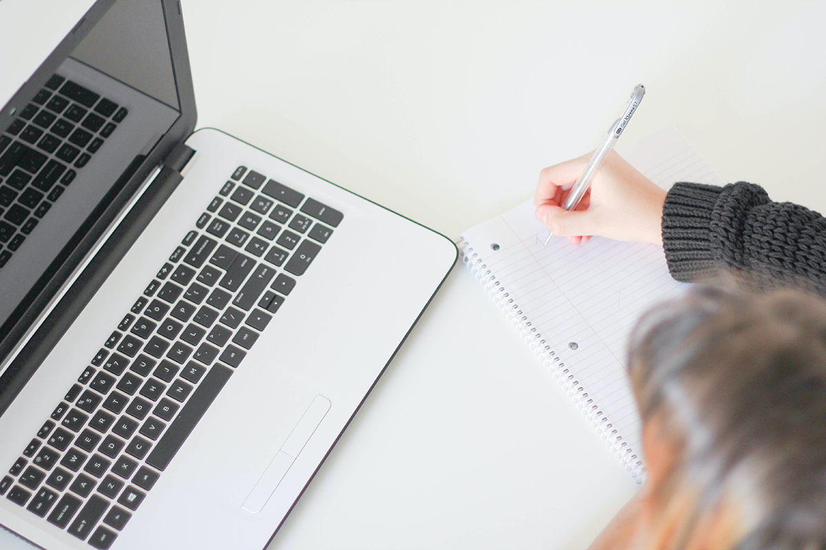 A young woman writes as she looks at a laptop