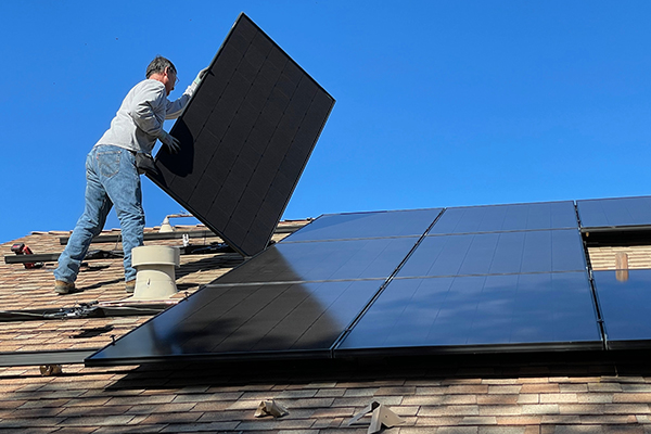A worker installs solar panels on the roof of a house.