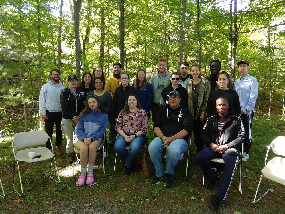 Students at Elbow Lake retreat September 2023, in two rows surrounded by green forest.