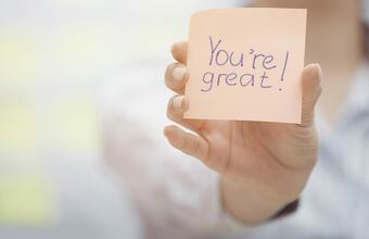 A person holds a post-it note that reads "You're Great!"