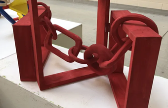 An art exhibit of a series of red chains linked through rectangular frames leading to colourful geometric shapes at the back.
