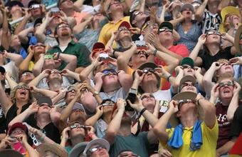 A crowd of people wearing eclipse glasses look up at the sun.