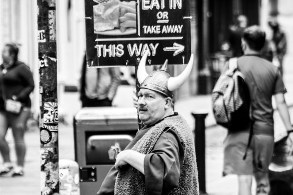 A photograph of a man standing on a city block wearing a viking-style helmet with two horns