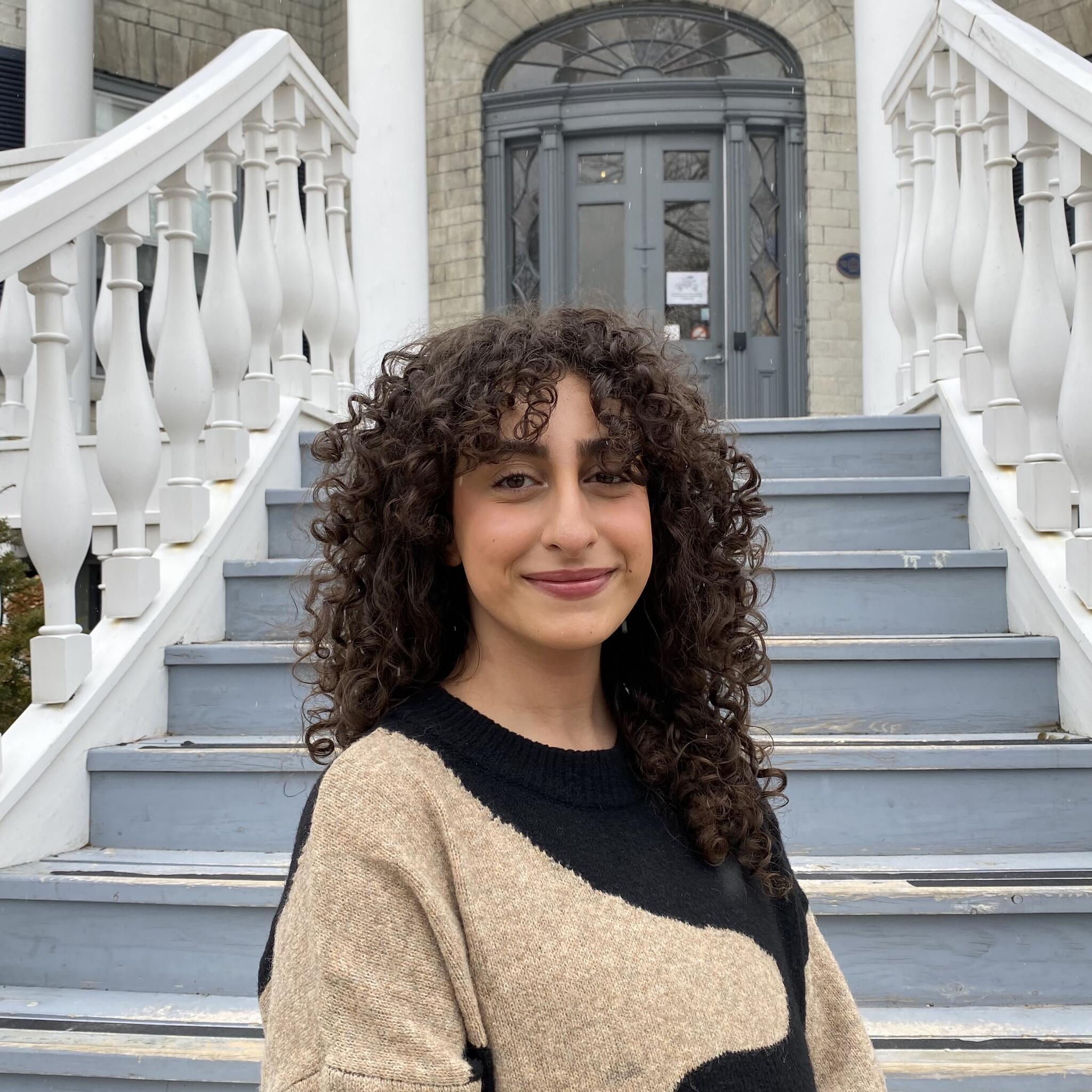 young smiling person with curly hair in front of stairs