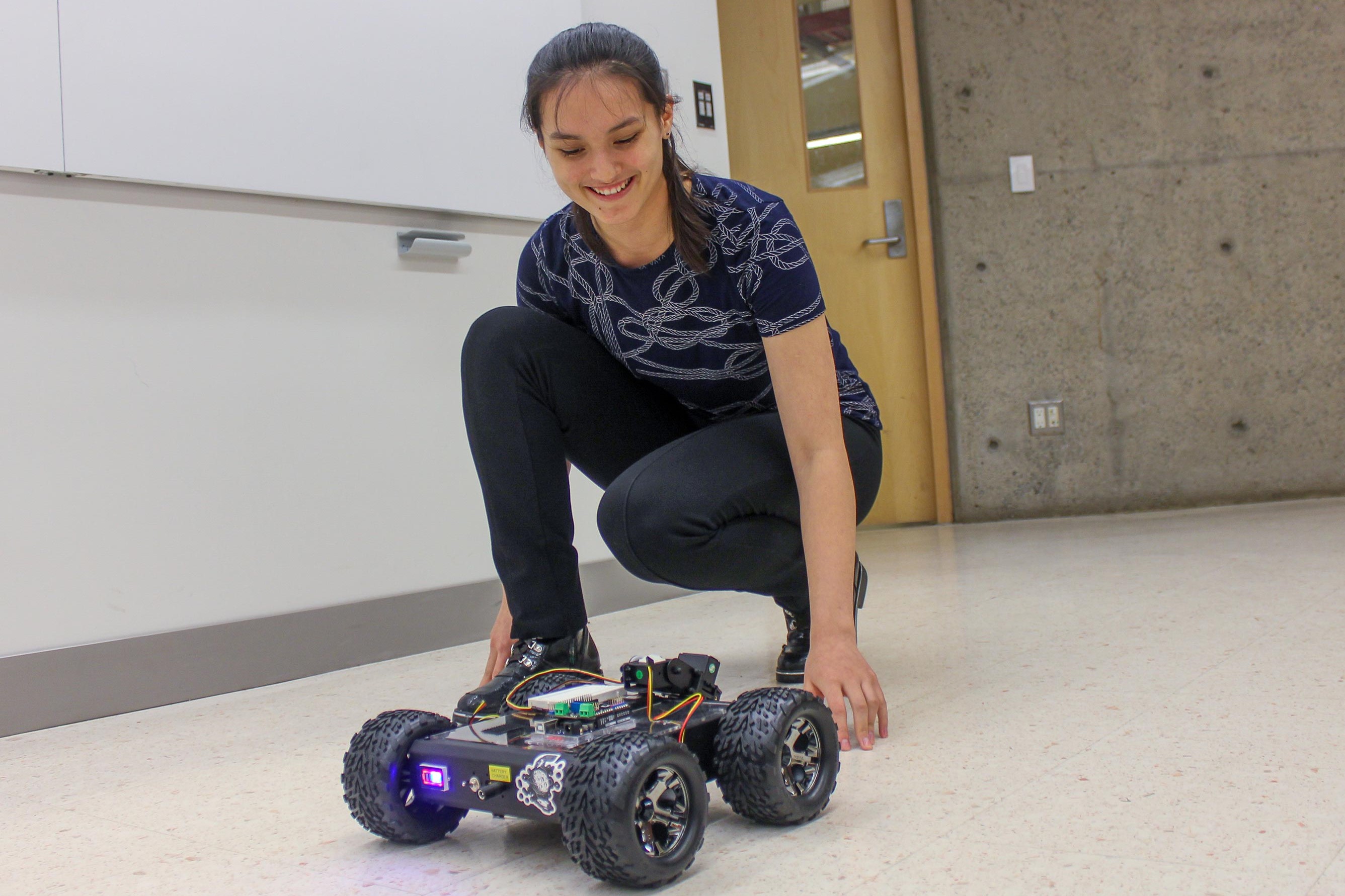 Student smiling next to small robotic vehicle