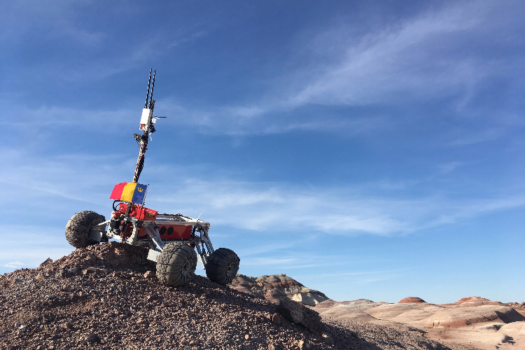 [A Mars rover built by Queen’s Space Engineering Team bearing a Queen’s University Tricolour flag at the Mars Desert Research Station in Utah. ]