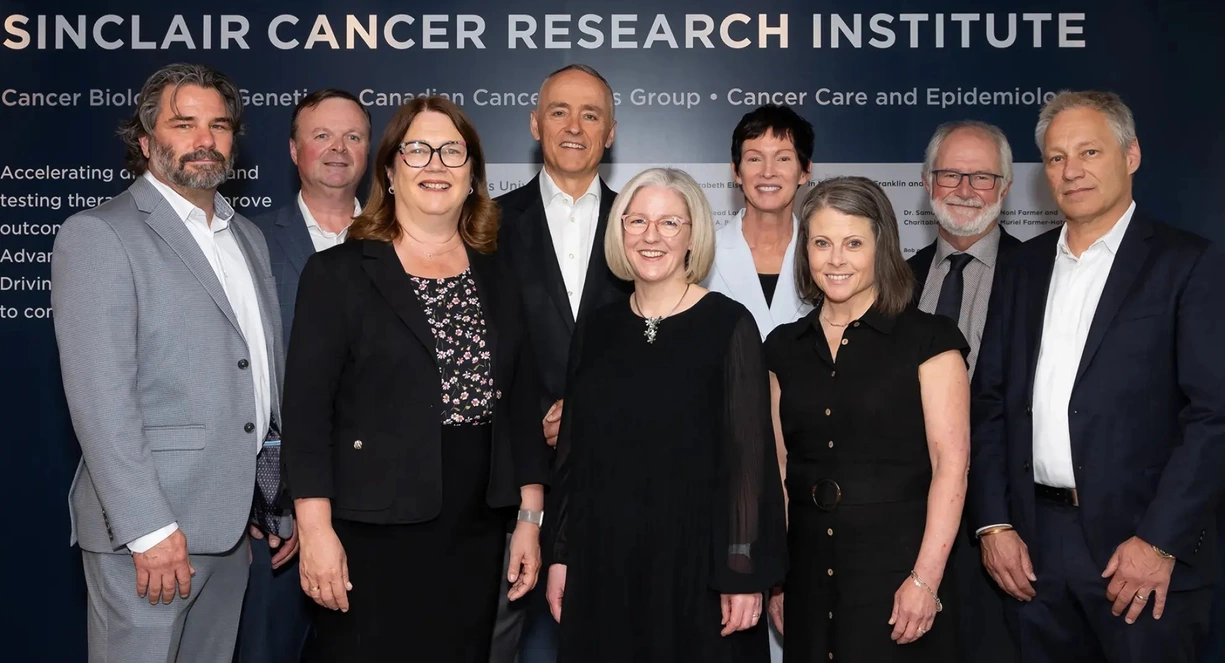 Nine people standing in front of the new Sinclair Cancer Research Institute sign